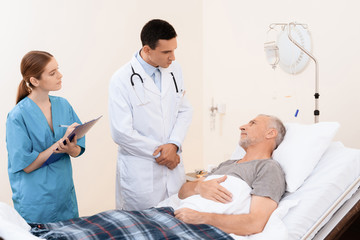 Obraz premium The old man lies on a cot in the medical ward. Next to him is a doctor and a nurse.