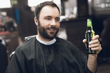 A man drinks alcohol in the hairdresser's armchair of a modern barbershop.