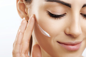 Closeup happy young woman applying cream to her face Skincare and cosmetics concept. Cosmetics. Woman face skin care.Natural makeup, touching face.
