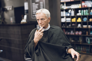 The old man drinks alcohol in the barber's chair in barbershop.