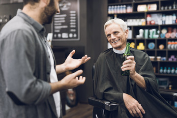 The old man drinks alcohol in the barber's chair in barbershop.