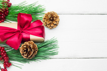 Gift box with red ribbon bow and branch christmas tree with cone on white wooden vintage background