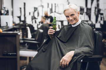 Fototapeta na wymiar The old man drinks alcohol in the barber's chair in barbershop.