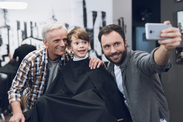 Adult man makes selfie on a smartphone with older men and boy in barbershop.