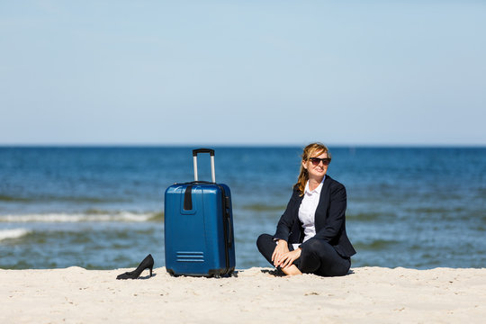 Woman sitting on suitcase on beach