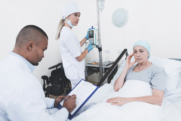 Obraz premium The nurse sets the woman a dropper. Nearby is a doctor who records the testimony of a woman who has cancer.