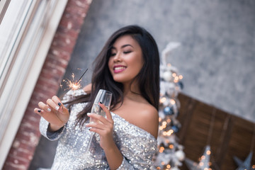 Beautiful girl with a fireworks in her hand dancing on the club, fun and waiting for Christmas time. Ready to celebrate. Confetti and fireworks. Christmas party