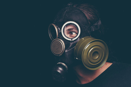 Post apocalyptic survivor man in gas mask on black background, scary eyes