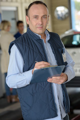 mechanic with a clipboard and pen standing near car