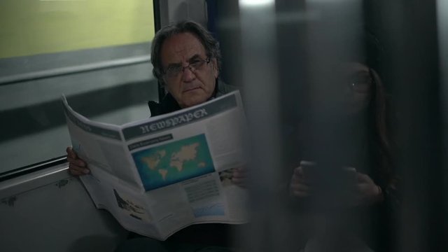 Passengers reading newspaper and using digital tablet in metro