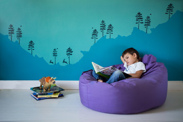 Toddler boy reading a book in a bright turquoise room
