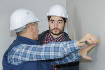 builder showing apprentice how to work on a wall