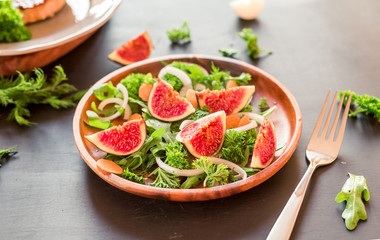 Autumn salad of arugula, figs in a brown earthenware plate on a dark background. top view