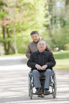 elderly woman pushing man in wheelchair