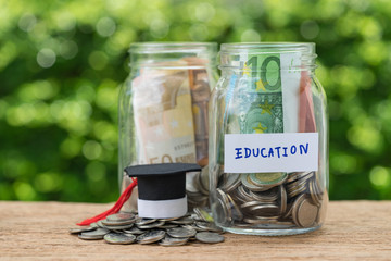 glass jar bottles with full of coins labeled as Education and graduates hat on stack of coins using as education or savings concept