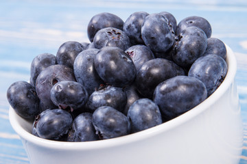 Fresh blueberries in glass bowl on blue boards, natural source of minerals, healthy dessert concept