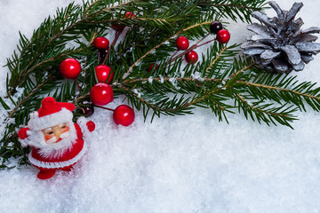 Figurine of Santa Claus against the background of a green spruce branch of the holly-berries.