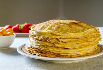 Pile of just made hot Russian pancakes or blini with berries.