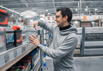 male customer buying car battery n the car supermarket. Difficult decision which battery to buy. He looks happy