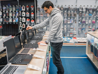Smart modern male customer choosing laptop in the computer shop. difficult decision. He is opening...