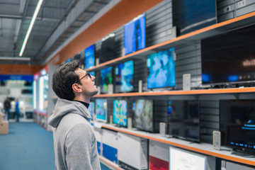 Smart modern male customer choosing large TV-sets at electronics store. He looks wondered. New...
