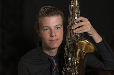 Fototapeta premium Close up of young man with saxophone on black background
