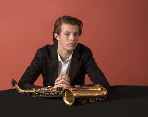 Young man with saxophone looking at camera, red background