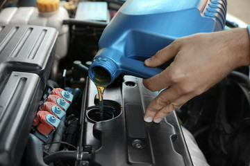 Young male mechanic pouring engine oil from canister, closeup