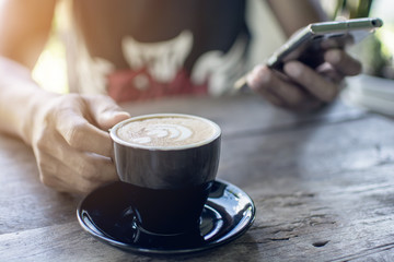 Hand of man holding a hot of coffee cup and mobile phone on the wooden table