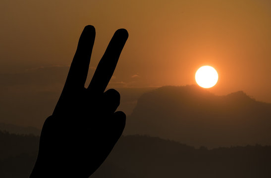 Silhouette of two fingers of woman’s hand or victory sign on the mountain landscape during sunset, number two