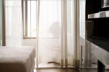 a lonely girl sitting behind sheer curtain in clean white room with sad heart broken and loneliness emotion after break up.