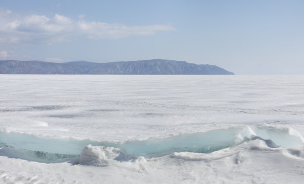 Transparent blue ice hummocks on lake Baikal shore. Siberia winter landscape view. Snow-covered ice of the lake. Big cracks in the ice floe.