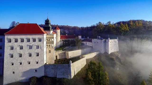 Historic Renaissance castle Pieskowa Skala on a steep cliff near Krakow in Poland in morning fog.  Aerial flyby video in fall