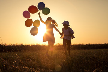 Silhouette of two happy children which playing on the field at the sunset time. © altanaka
