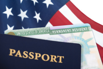 United States of America permanent resident card, green card, displayed with a US flag in the background and a passport in the foreground. Immigration concept.