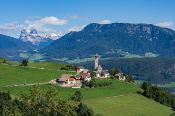 View Alpine village with church and buildings at summer day, Dolomites mountains background.  Soprabolzano, Oberbozen, South Tirol, Italy.
