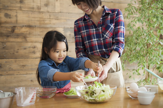 Cute Little Girl And Her Beautiful Mom.
They Are Smiling While Cooking In Kitchen At Home.