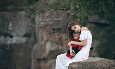 Young model-looking woman sitting on the rocks with a doll on her lap. A teenage girl imagines that...