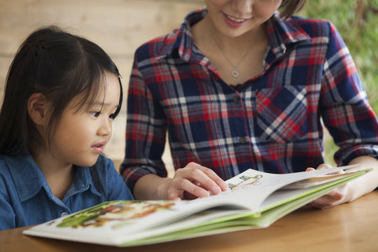 A young mother and a girl read a picture book together.