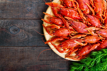 A  pile of tasty boiled crawfish on a round wooden tray on a dark table. Top view. Free space for an inscription.