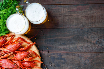 A  pile of tasty boiled crawfish on a round wooden tray and two mugs of cold beer on a dark background. Top view. Free space for an inscription.