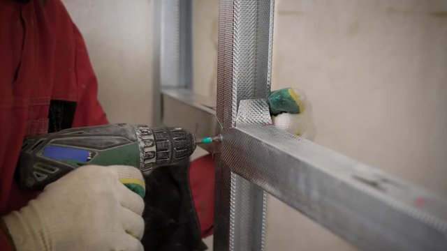 man is using electrical screwdriver, twisting bolts in aluminium structure during repair in home