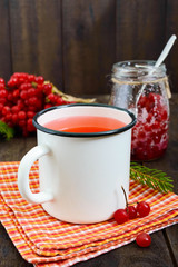 Hot berry tea in a white mug on a dark wooden background. Vertical view. Tea with viburnum. Berries with sugar in a glass jar. Therapeutic drink.