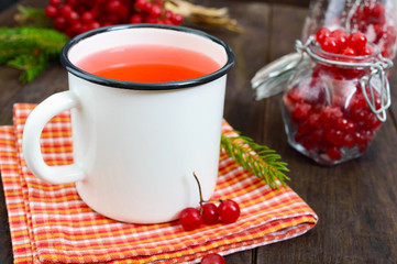 Hot berry tea in a white mug on a dark wooden background. Tea with viburnum. Berries with sugar in a glass jar. Therapeutic drink.