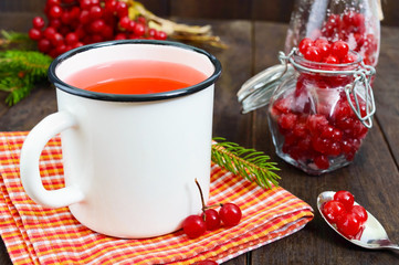 Hot berry tea in a white mug on a dark wooden background. Tea with viburnum. Berries with sugar in a glass jar. Therapeutic drink.