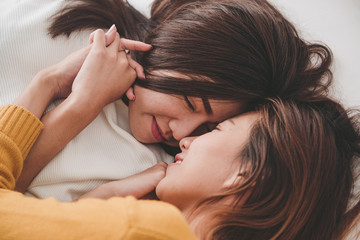 Fototapeta premium Top view of beautiful young asian women lesbian happy couple hugging and smiling while lying together in bed under blanket at home. Funny women after wake up. Lesbian couple together indoors concept.