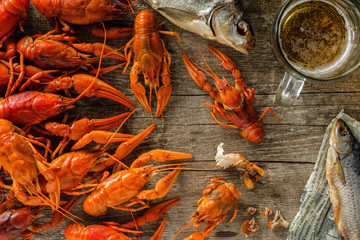 Fresh boiled crawfish and dried fish with a beer on a wooden table.