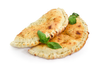 Two cooked calzone with basil twigs on a white background