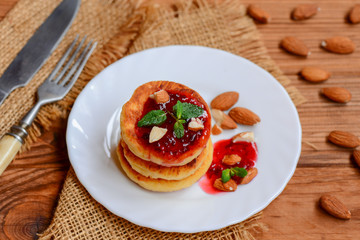 Fototapeta na wymiar Fried cottage cheese pancakes with berry jam, almonds and mint on a white plate. Syrniki recipe. Low carb cottage cheese pancakes