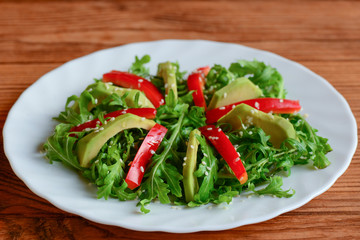 Avocado, arugula and pepper salad on a white plate. Simple arugula and avocado salad with red pepper and sesame seeds. Raw food menu. Closeup